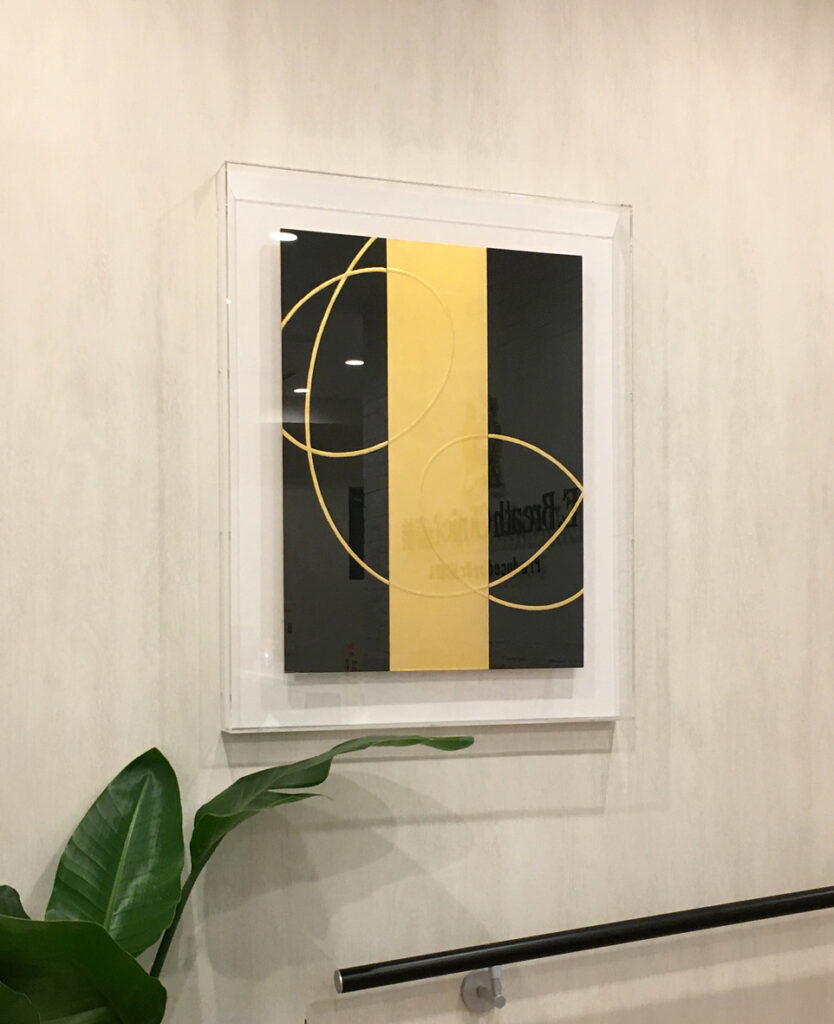 エントランスの壁面に飾られた中澤愼一の現代アート作品「ellipse」。アクリルボックス額装された金と黒の抽象画